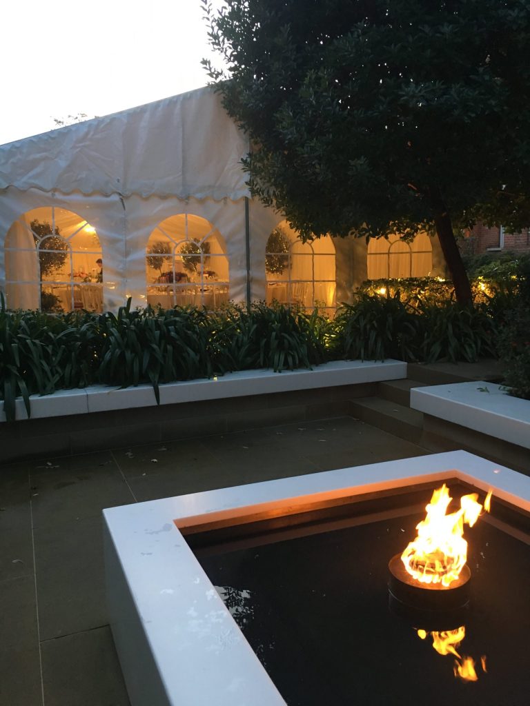 A large sheltered evening marquee used for a dining event, with an outdoor fire-pit