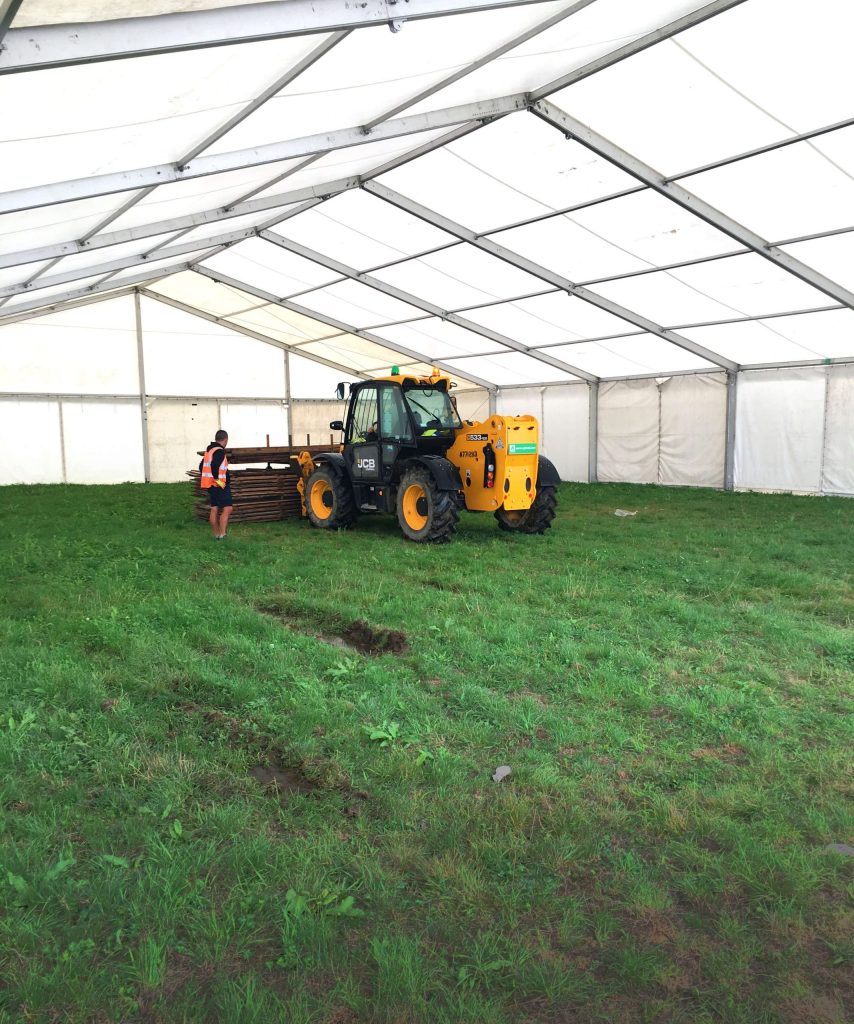 A tractor in progress of leveling the ground to add a wooden floor to a large outdoor marquee