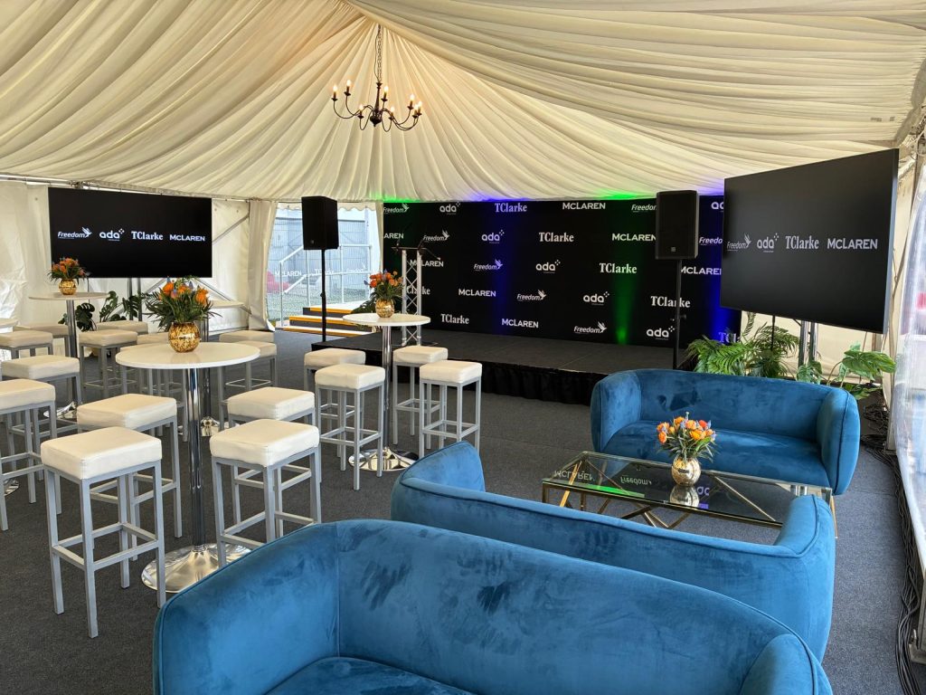 Marquee interior with blue velvet sofas, branded stage backdrop and poseur tables for a McLaren corporate event in London
